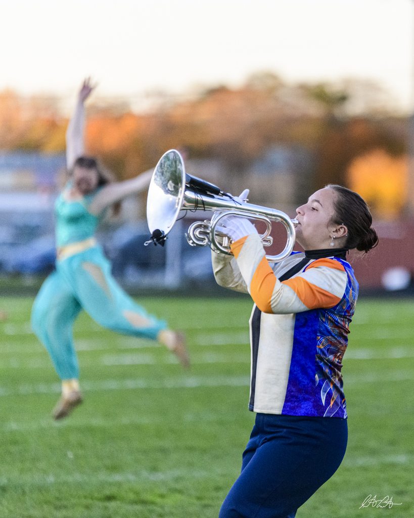 Shaelie performs on Mellophone while Madie executes a leap in the background.